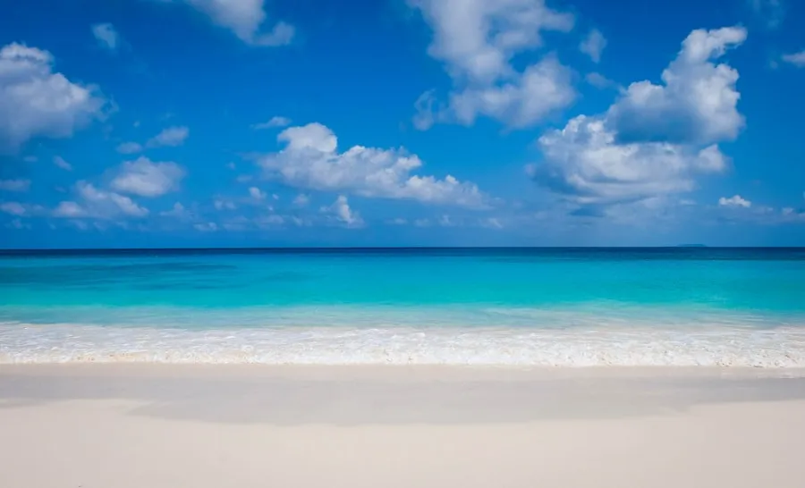 White-sand beach and blue ocean beneath a partly cloudy sky